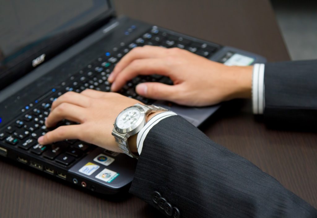 ノートパソコンのキーボードを打つスーツ姿の男性の腕の写真